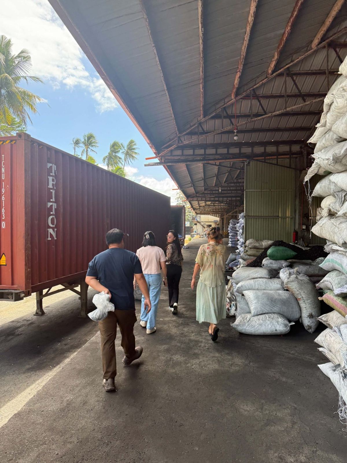 People walking past charcoal stock and a shipping container at a warehouse